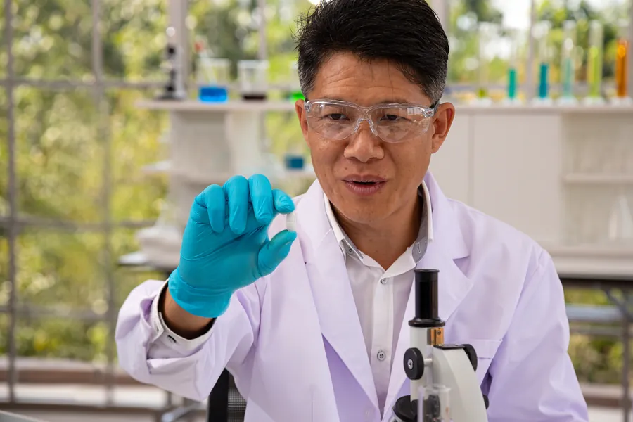 Scientist holding pill in laboratory research environment with microscope and scientific equipment